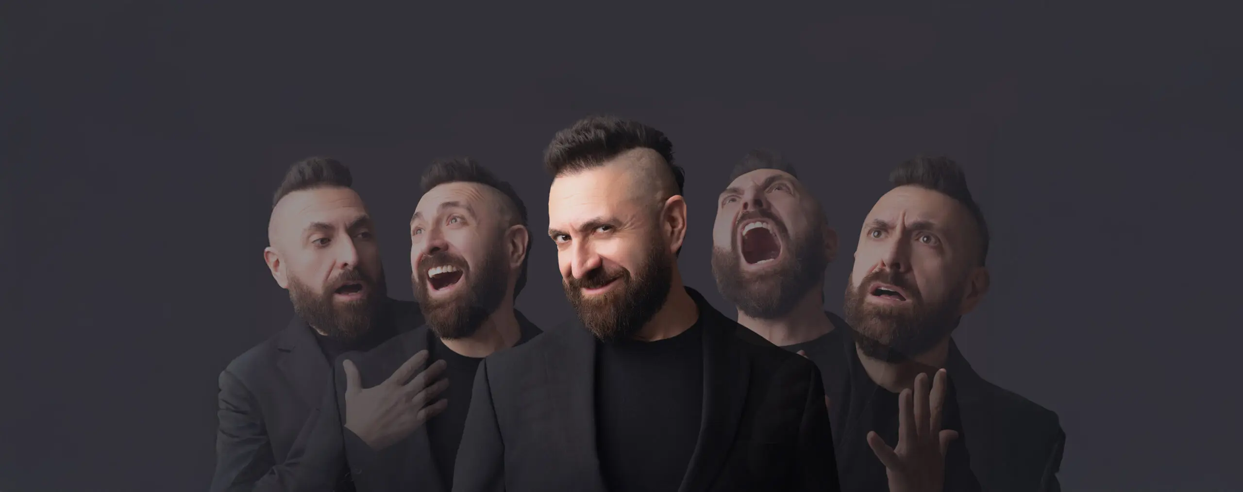 A composite image of lyric tenor Marcos Vigil. He is standing in front of a dark grey background lit by studio lighting from the front. He is wearing a black blazer jacket buttoned, and a black t-shirt underneath. He has a beard and his signature mohawk. In the middle, he is looking at the camera with his head tilted to the side, slightly turned to the right with a mischievous smile. Behind him are four more faded images which allow the dark background to filter through, two on the left and two on the right, which depict looks of shock, extreme happiness, an angry scream up toward the air, and a look of dispair.