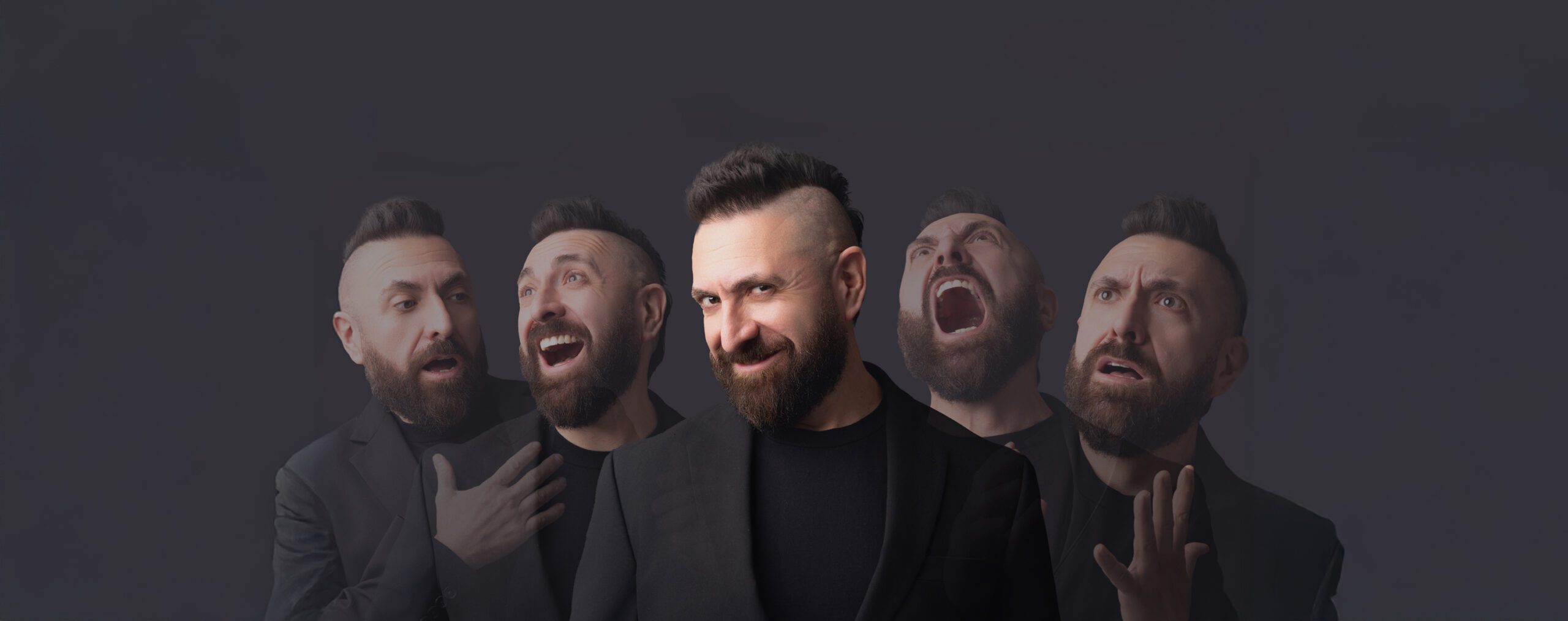 A composite image of lyric tenor Marcos Vigil. He is standing in front of a dark grey background lit by studio lighting from the front. He is wearing a black blazer jacket buttoned, and a black t-shirt underneath. He has a beard and his signature mohawk. In the middle, he is looking at the camera with his head tilted to the side, slightly turned to the right with a mischievous smile. Behind him are four more faded images which allow the dark background to filter through, two on the left and two on the right, which depict looks of shock, extreme happiness, an angry scream up toward the air, and a look of dispair.