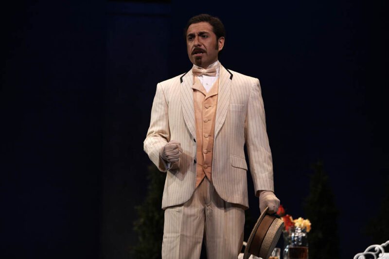 Marcos Vigil, Tenor, wearing a light peach colored suit with pinstripes, a peach colored waistcoat with a matching bow tie, and light colored gloves.